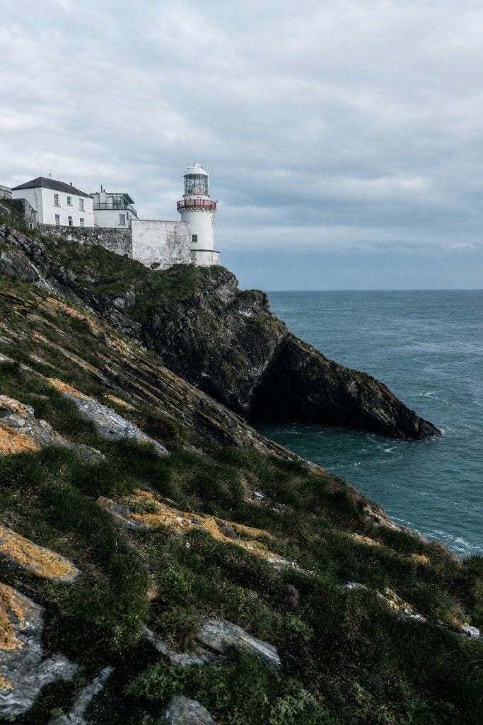 The working Wicklow Head lighthouse and its white buildings above a rock arch.